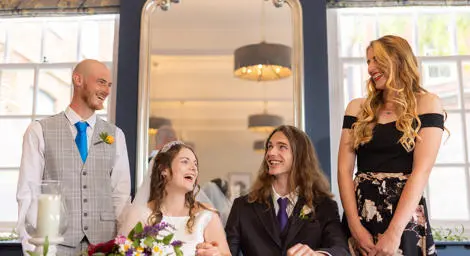 Young wedding couple holding hands with groom smiling at his best man.