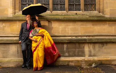 Indian couple looking up and smiling outside with groom holding an umbrella 