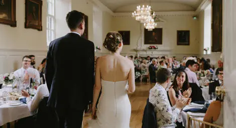 Bride and groom walking into wedding breakfast reception with guests clapping.