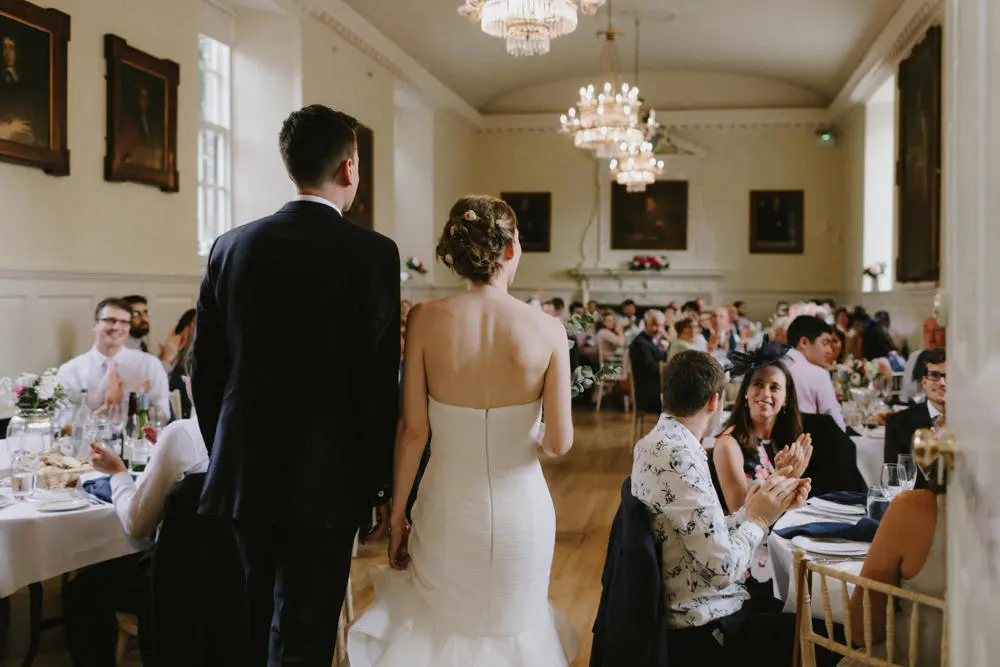 Bride and groom walking into wedding breakfast reception with guests clapping.