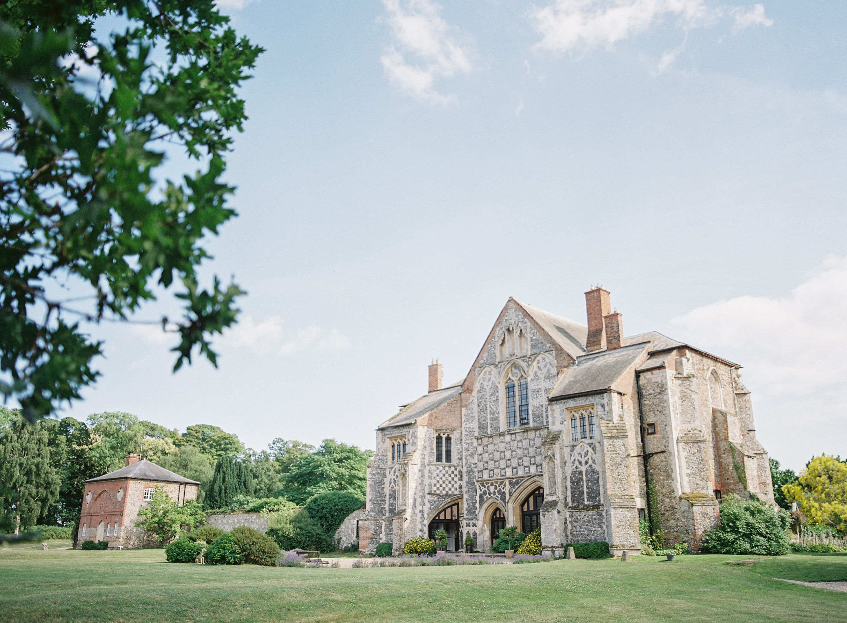Butley Priory set in manicured gardens and trees behind. 