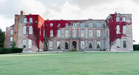 Outside of Glemham Hall with grass in front and red vines growing on the building.