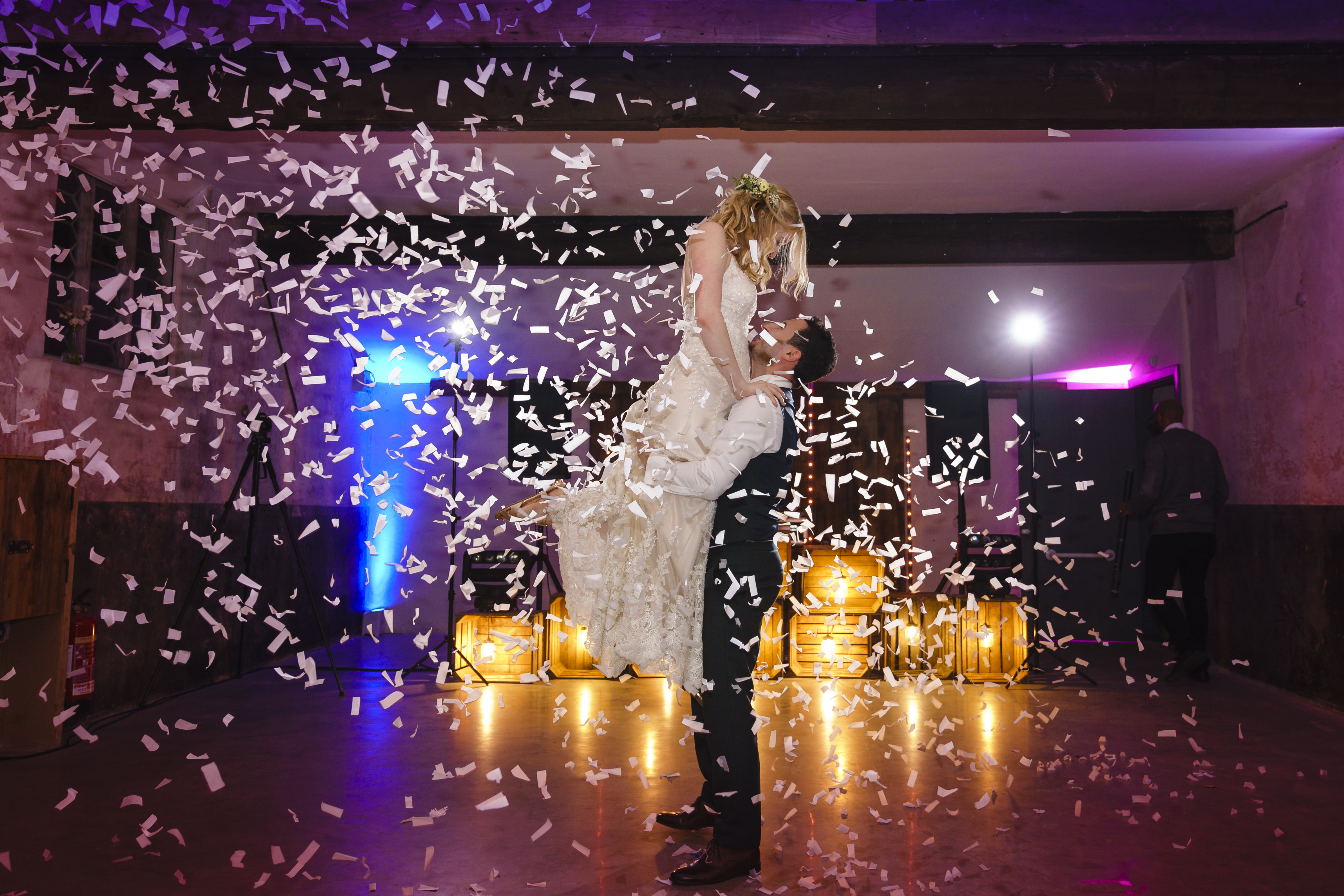 Groom lifting bride into the air at their first dance with confetti surrounding them.