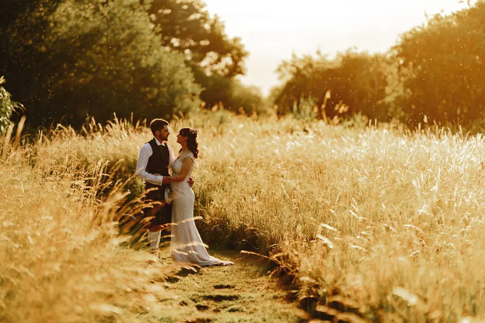 Bride and groom holding hands in a field with the sun setting.