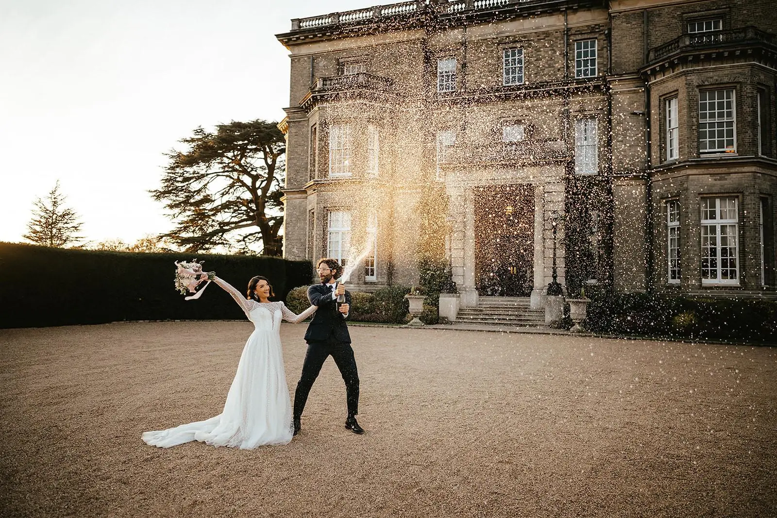 Bride and groom spraying champagne outside venue