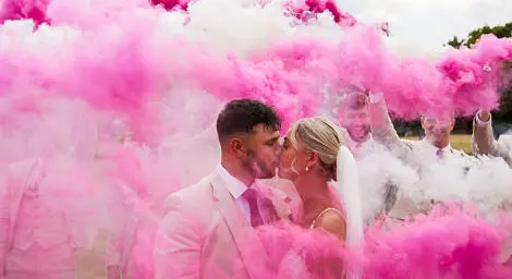 Bride and groom kissing amongst pink flares