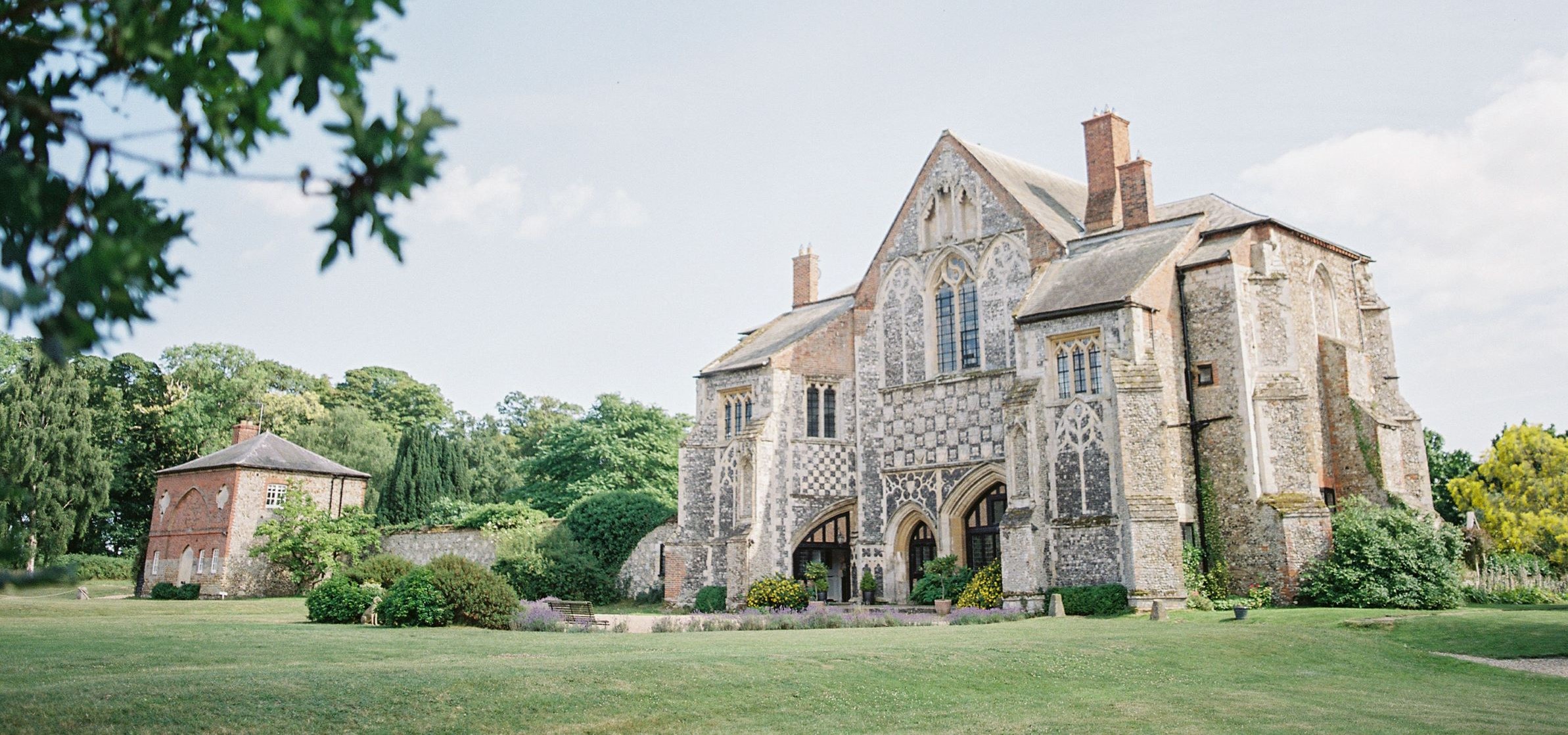 Butley Priory set in manicured gardens and trees behind. 
