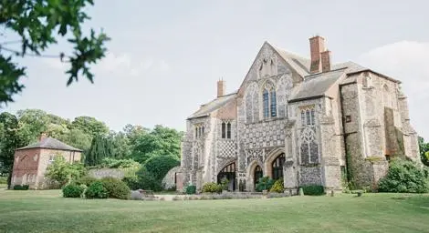 Butley Priory set in manicured gardens and trees behind.