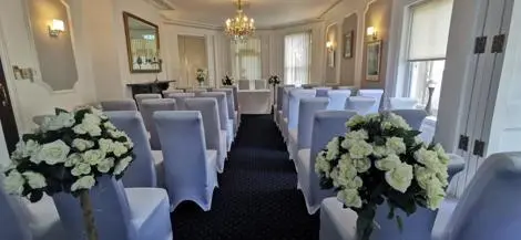 Chairs with white covers facing forwards. White roses at the top of the wedding aisle. 