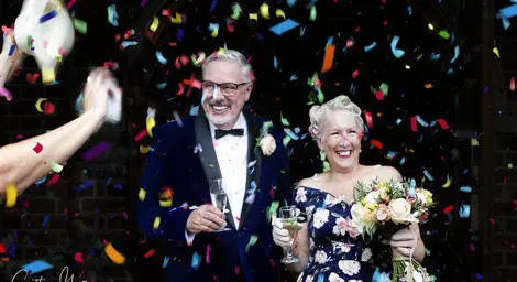 Older couple on their wedding day in a shower of colourful confetti with champagne