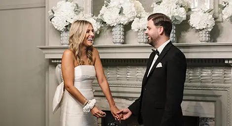 Bride and groom in front of fireplace, beaming at each other