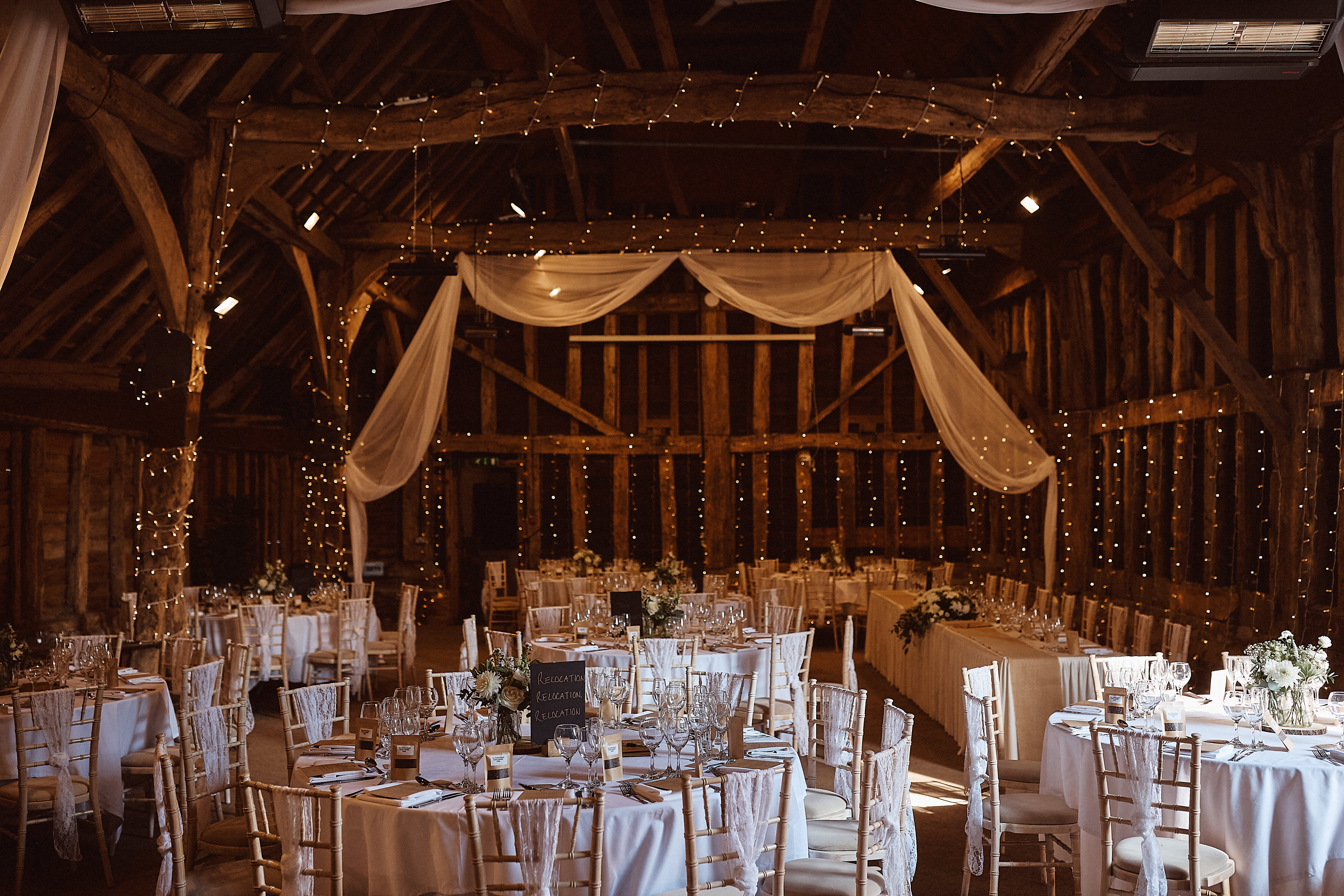 Inside a barn with fairy lights and tables set up for a wedding. 