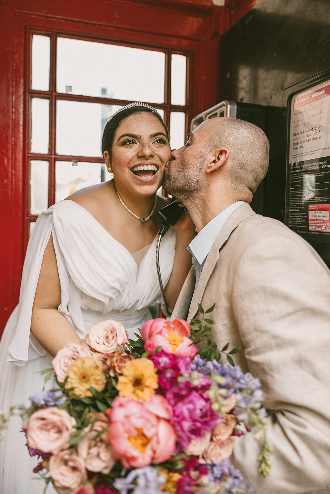 Groom kissing smiling bride in a red phone booth