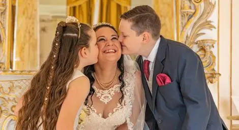 Boy and girl kissing their mum at her wedding