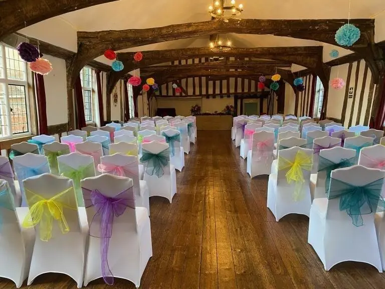 Yellow, purple, green, pink and blue ribbon tied into bows on white chairs.