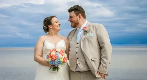 Bride and groom by the seaside smiling at each other
