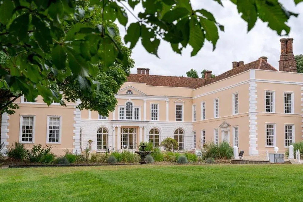 Outside of Hintlesham Hall with green shrubbery and gardens in front.
