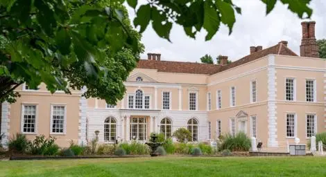 Outside of Hintlesham Hall with green shrubbery and gardens in front.