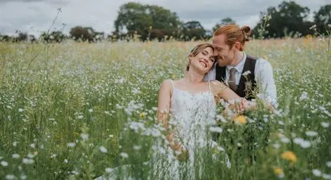Bride and groom sitting together in a meadow smiling blissfully - Photography by Jackie Gilman Photography