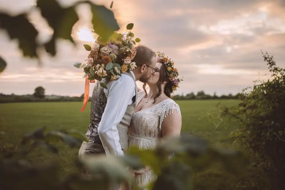 Bride and groom with beautiful flowers kissing in meadow