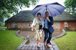 Man holding umbrella with a woman holding a toddler in the rain.