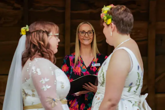 Two brides getting married looking and smiling at their registrar. 
