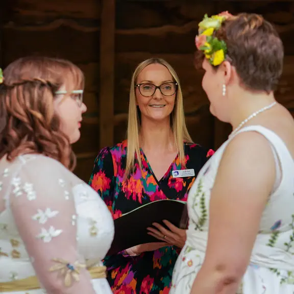 Two brides getting married looking and smiling at their registrar.