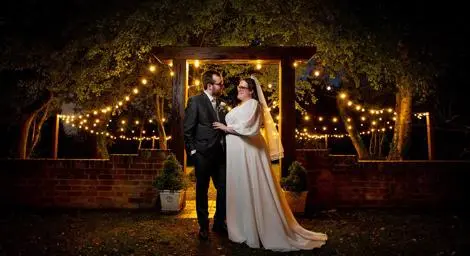 Bride and groom at night under a lit arbour