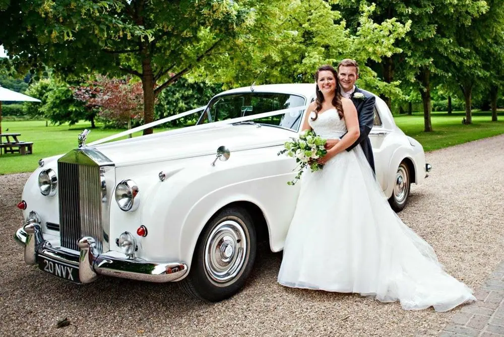 Bride and groom posing in front of beautiful white Rolls Royce