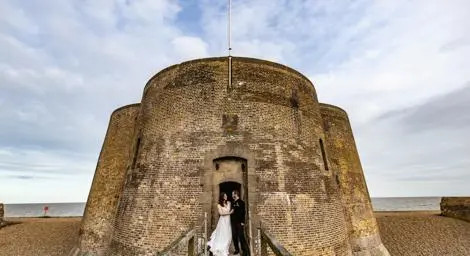Bride and groom in front of a Martello Tower on the beach