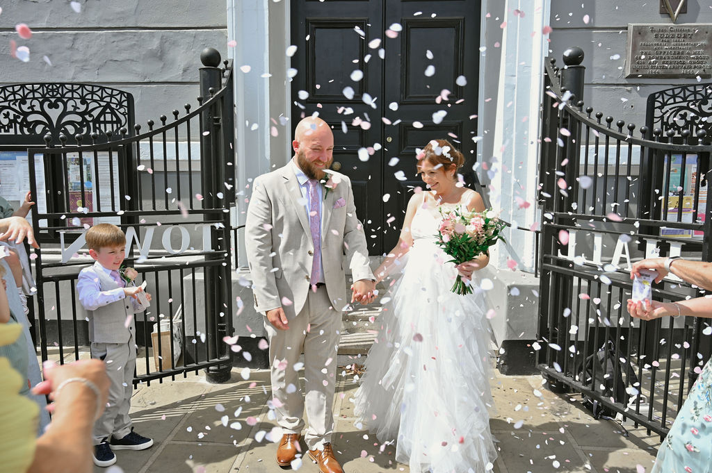 Bride and groom celebrating in a shower of petal confetti outside Sudbury Town Hall