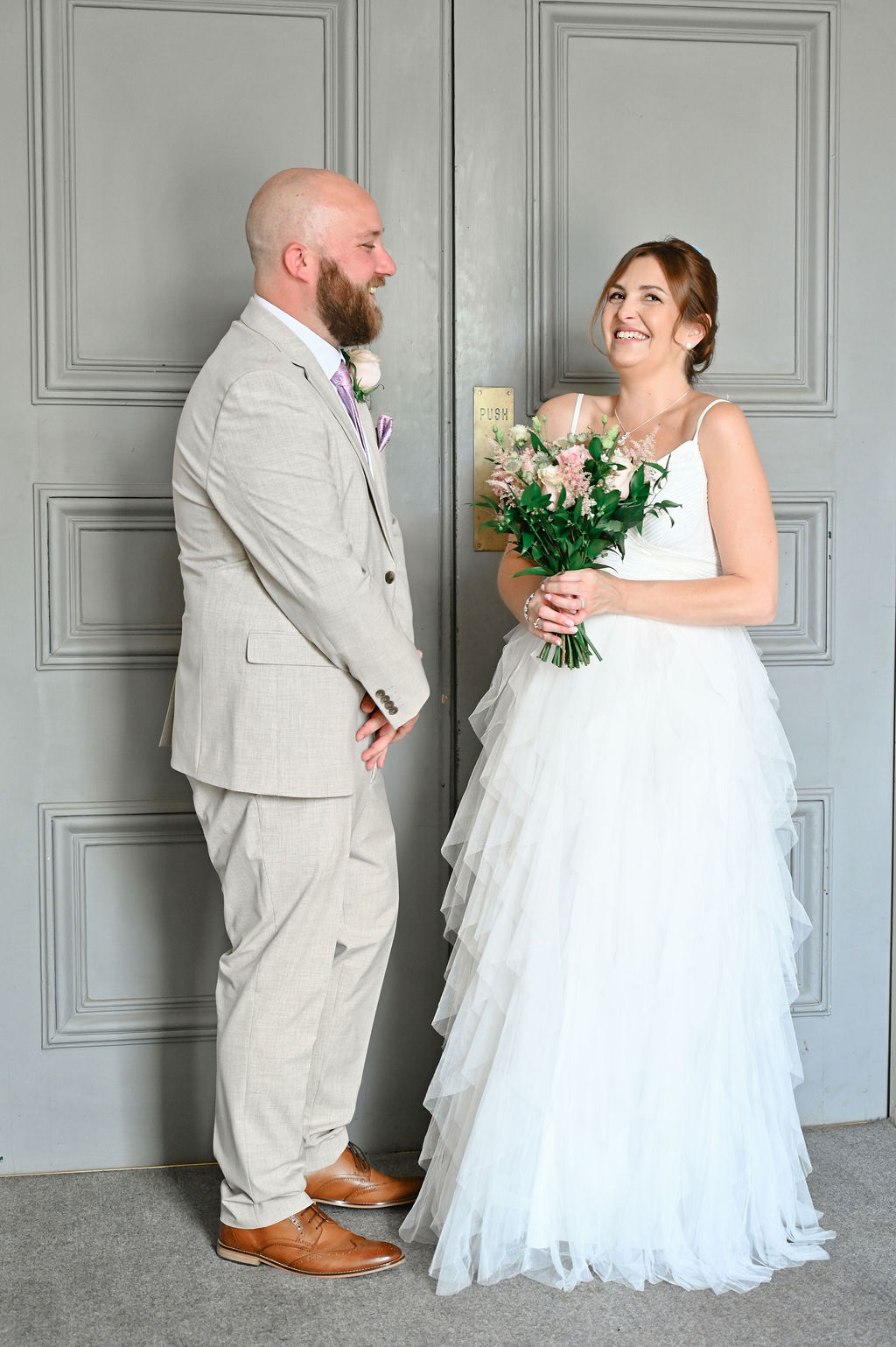 Bride and groom smiling at each other in front of elegant grey doors at Sudbury Town Hall