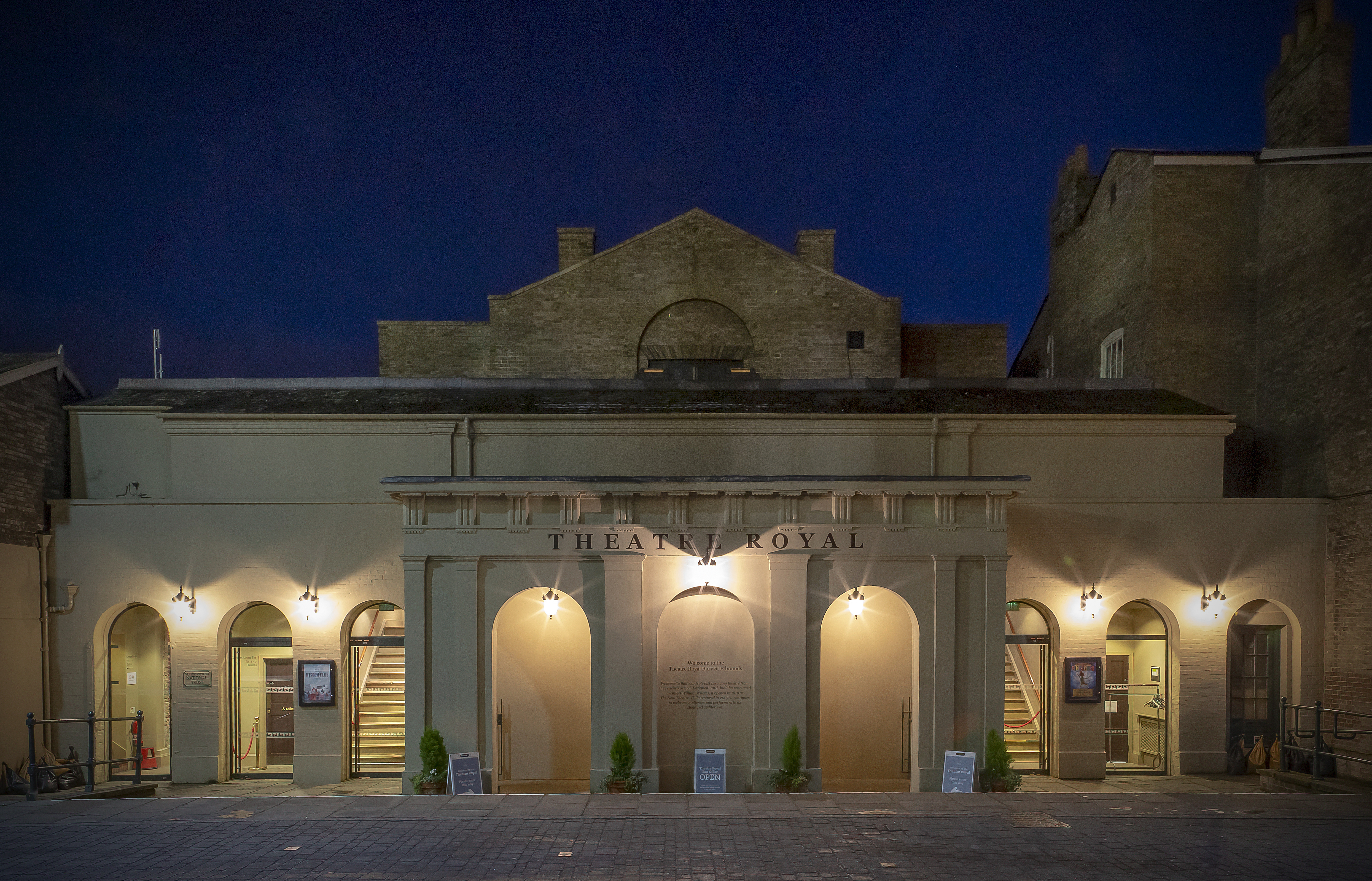 Outside the Theatre Royal at night with lights shining across the building.