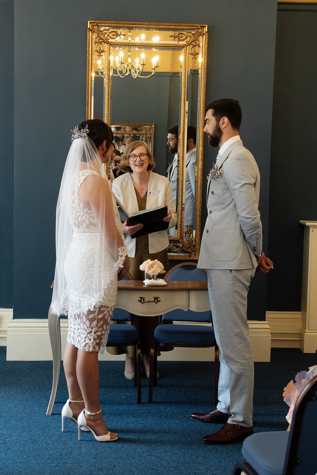 Wedding ceremony at the Pickwick Room at Ipswich Town Hall. Bride and Groom with Suffolk Registrars Celebrant in front of mirror and table