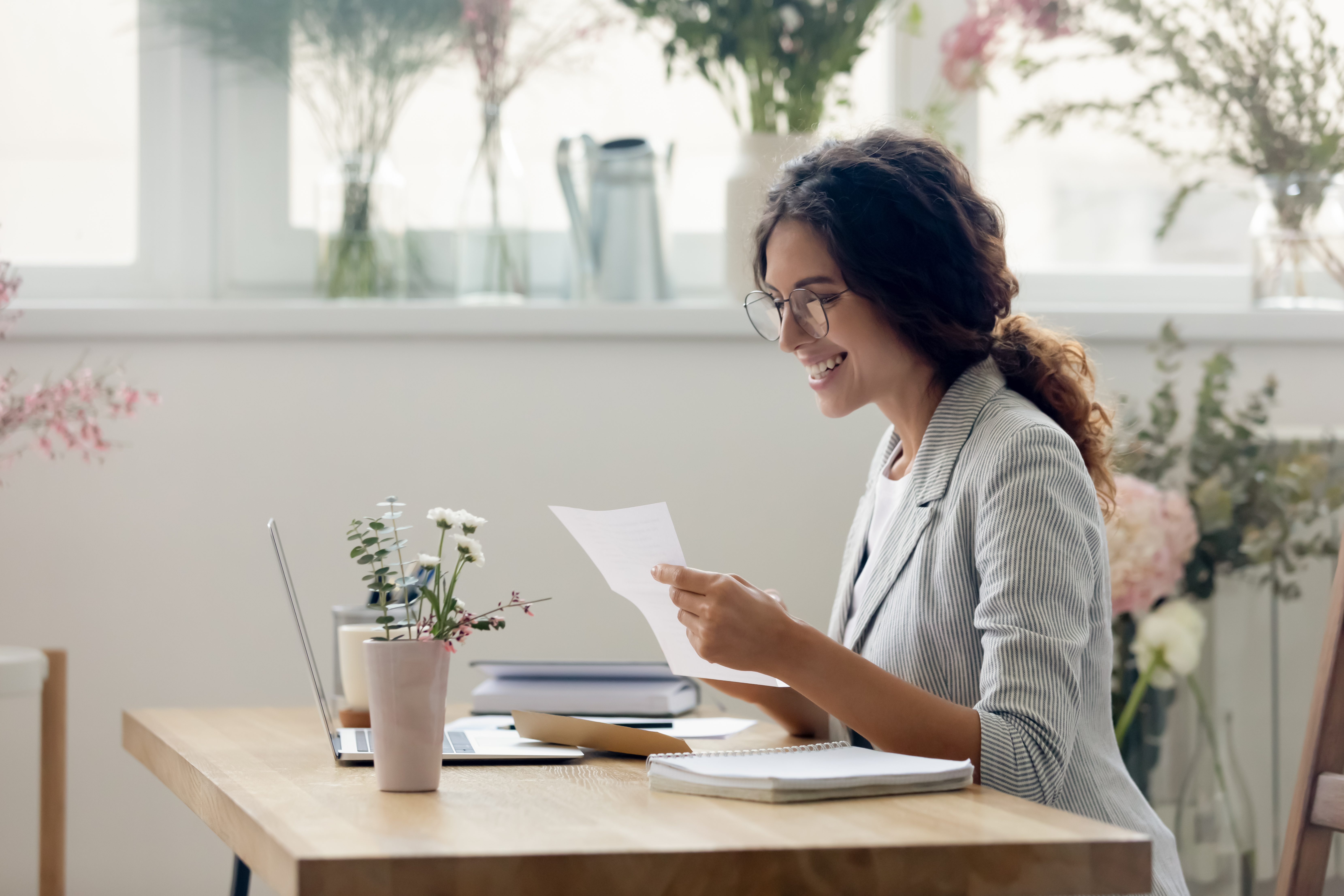 Young professional woman sitting at desk reading a piece of paper, smiling
