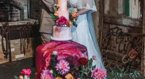Bride and groom in rustic stable setting cutting a three tier cake